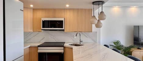 A modern kitchen with a marble countertop, wooden cabinets, a built-in oven, and a microwave.