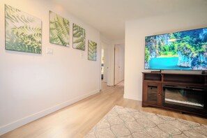 Ein Flur mit einem Flachbildfernseher auf einem Holzständer, einem gemusterten Teppich und drei Bildern mit Farnmotiven an der Wand.