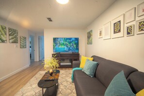 Ein Wohnzimmer mit einem dunkelbraunen Sofa, einem Couchtisch und einem an der Wand befestigten Flachbildfernseher.
