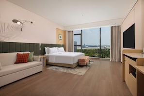 Habitación de hotel con cama, sofá, televisor y vista al aeropuerto.