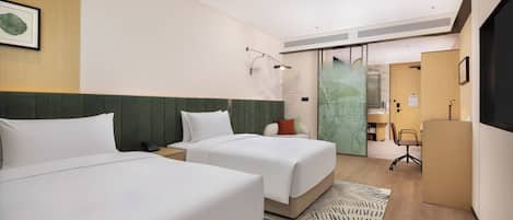 Habitación de hotel con dos camas, un escritorio, una silla, un mural con un mapa y una puerta que da a un baño.