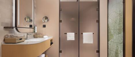 A modern bathroom with a curved vanity, a large mirror, and a glass door leading to a shower area.