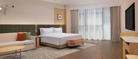 Quarto de hotel com cama, sofá, mesa pequena, televisão e janela com cortinas.