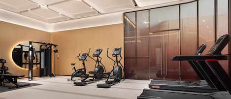 Un gimnasio moderno con equipo de cardio, un televisor montado en la pared y un espejo grande.