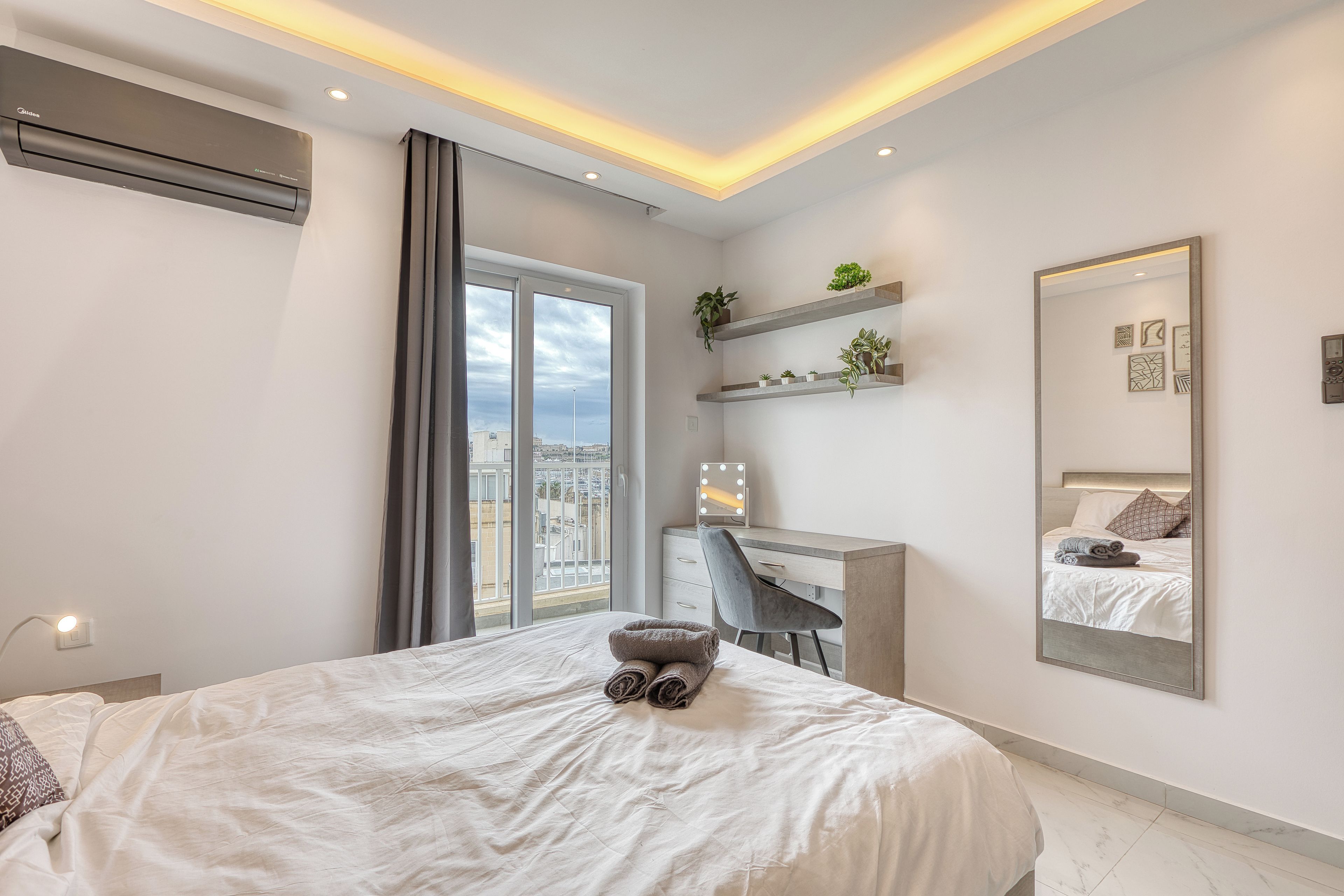 A modern bedroom with a bed, a desk, and a large mirror.
