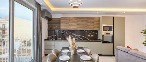 A modern kitchen with a dining area, large windows, and a view of the city.
