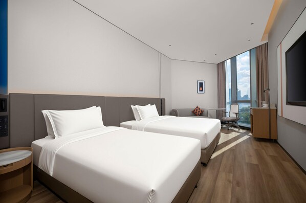 A hotel room with two beds, a desk, a chair, a TV, and a large window with a city view.