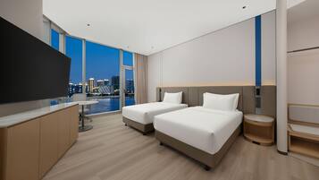 A hotel room with two beds, a desk, a TV, and a city view.