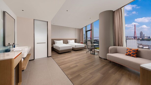 A modern hotel room with a large window, a sofa, two beds, a desk, and a bathroom. - Holiday Inn Express Shanghai North Bund Riverside (Shanghai)