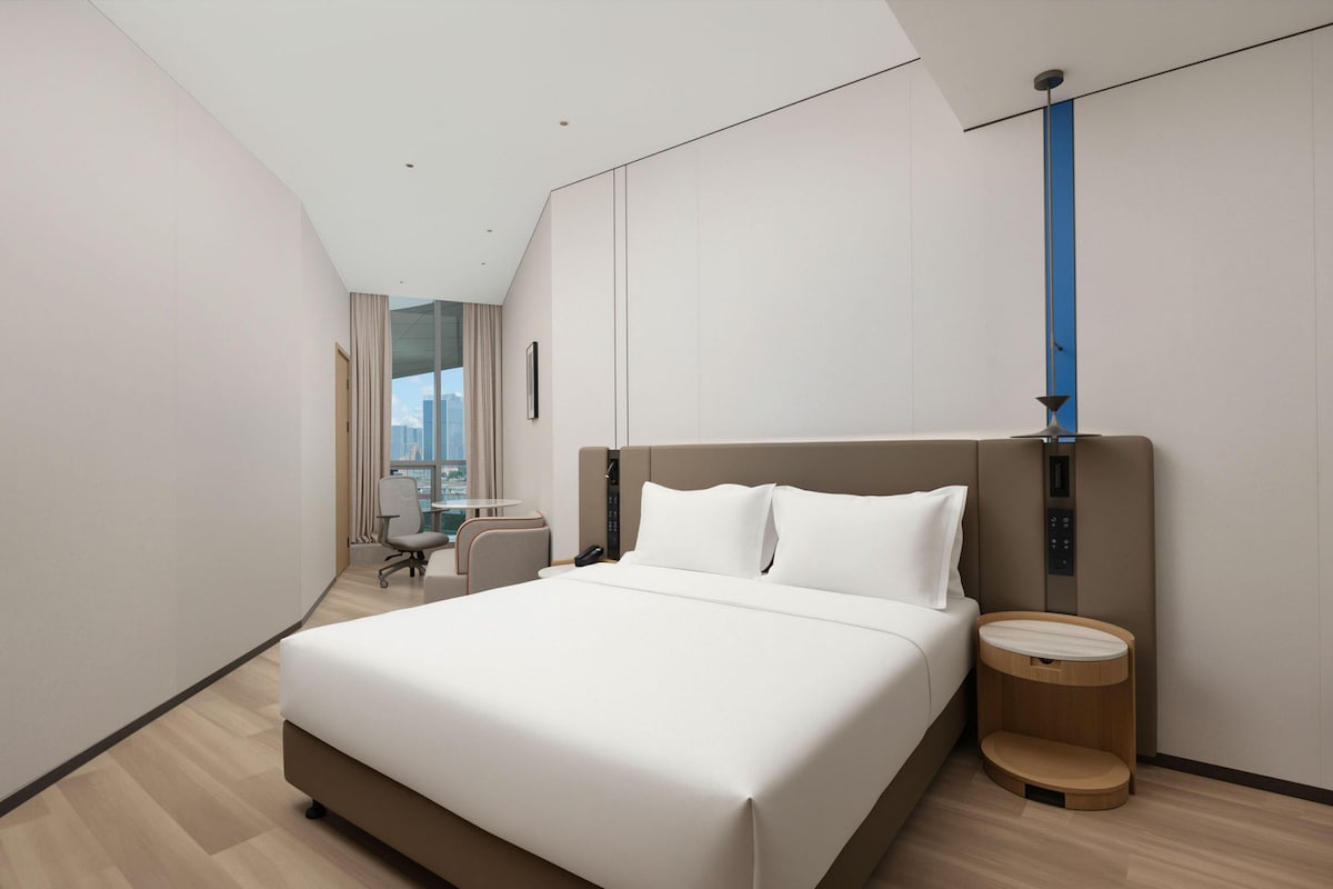 A modern hotel room with a large bed, a desk, and a view of the city.