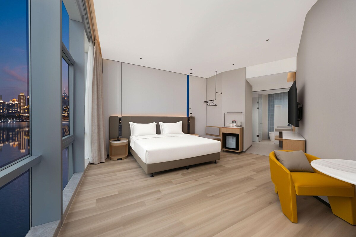 A modern hotel room with a large bed, a small desk, a chair, and a TV.