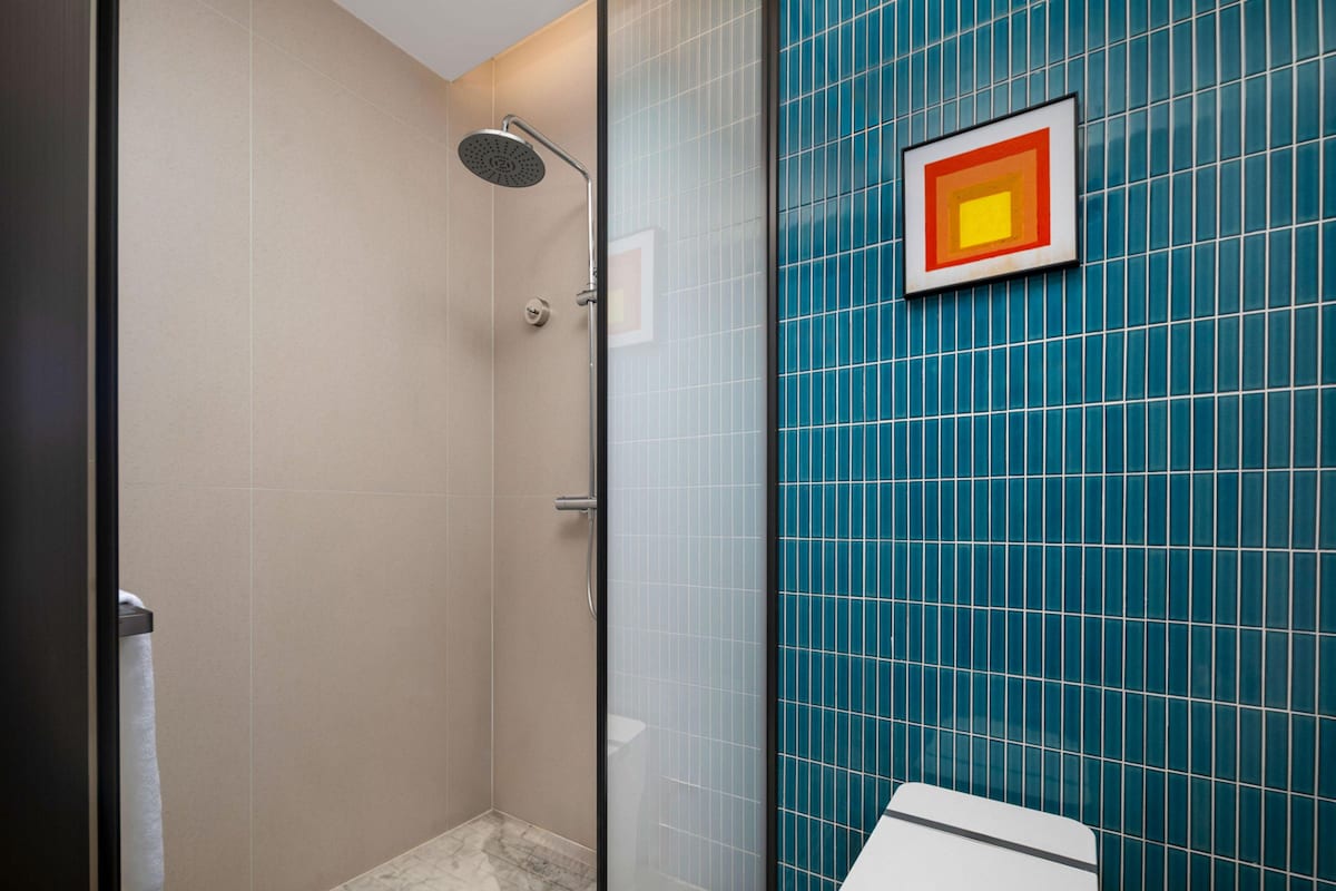 A modern bathroom with a glass shower enclosure, a toilet, and a wall with blue tiles.