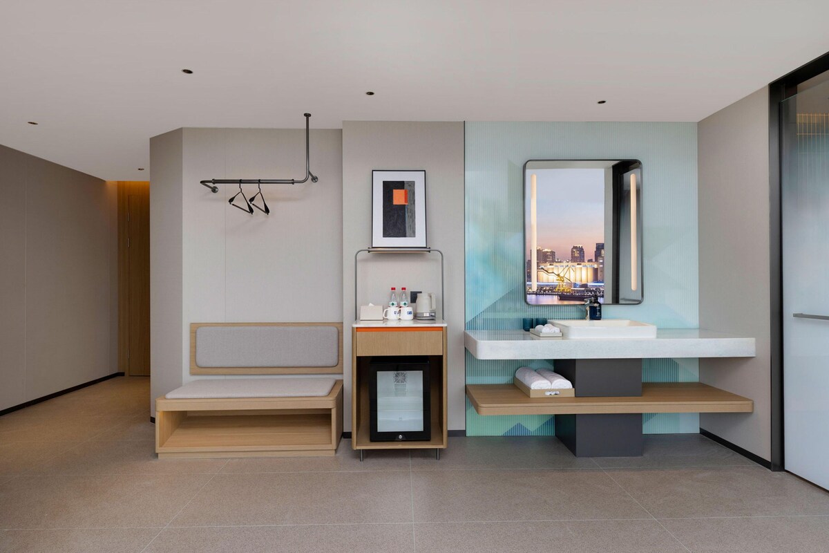 A modern bathroom with a bench, a sink, a mirror, and a framed picture.