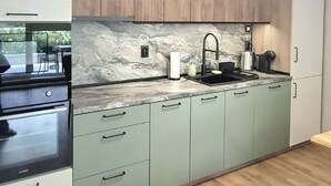 Una cucina moderna con mobili color verde chiaro, zoccolo in marmo e soffitto in legno.