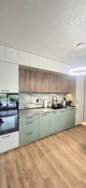 A modern kitchen with light green cabinets, a marble backsplash, and a wooden ceiling. - Stylish Apartment with Large Green Terrace & Private Parking (Sofia)