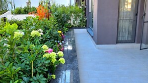 Un edificio moderno con una galleria coperta, un giardino ricco di piante e fiori, e un cielo sereno.