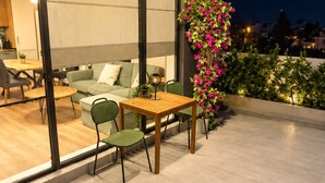 Una terrazza esterna con tavolo e sedie, un divano verde e un vaso con fiori rosa.