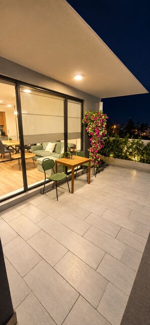 An outdoor patio with a dining table and chairs, a green sofa, and a potted plant with pink flowers. - Stylish Apartment with Large Green Terrace & Private Parking (Sofia)