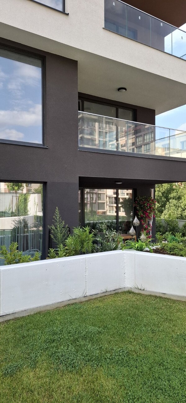 A modern two-story building with a balcony, large windows, and a landscaped garden area.