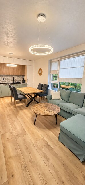 A modern living room with a wooden floor, a round coffee table, a sofa, and a dining table with chairs.