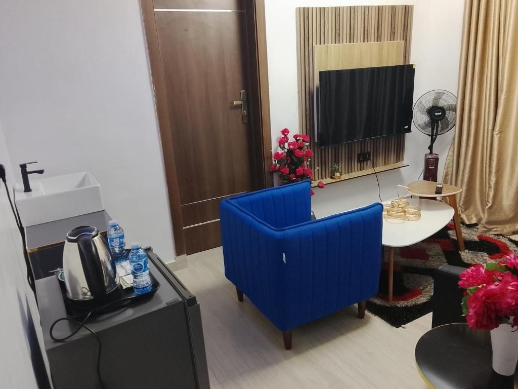Una habitación pequeña con un sofá azul, un escritorio con un ventilador, un televisor y una puerta.