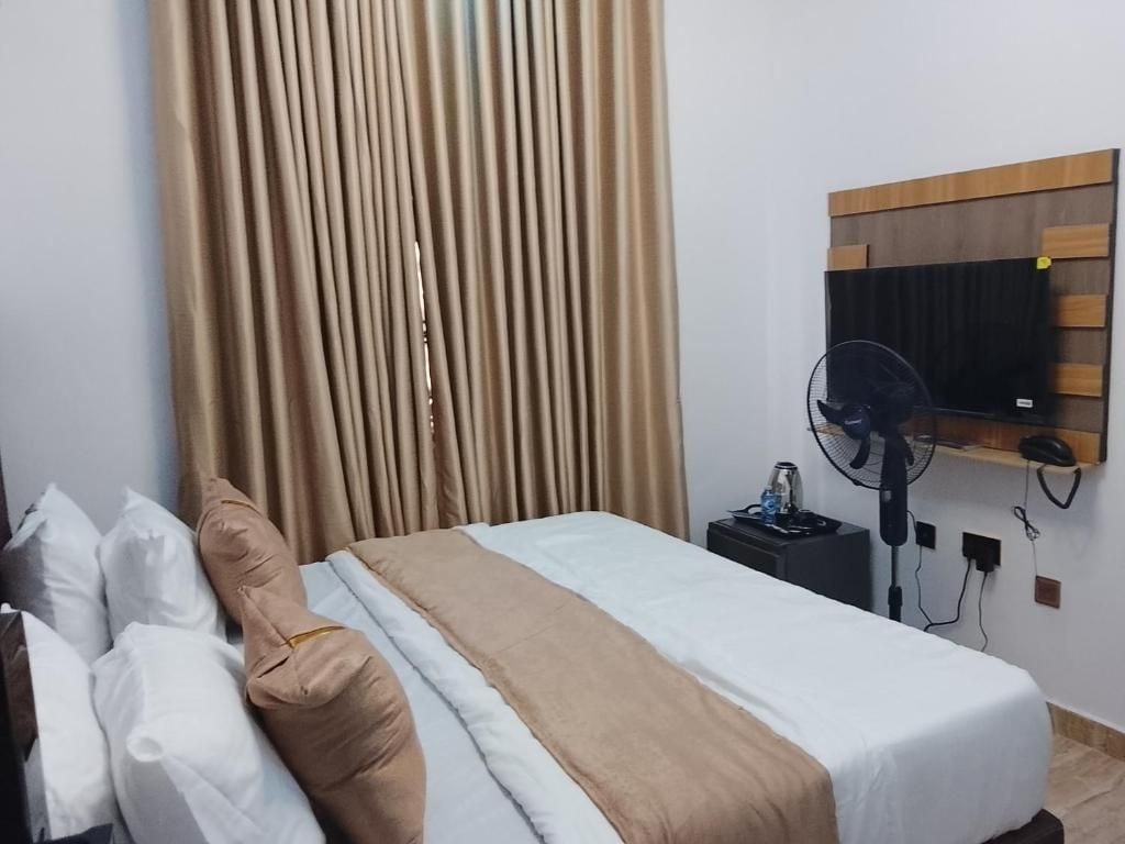 Une chambre d’hôtel avec un lit, une table de chevet avec un ventilateur, un téléviseur fixé au mur et un rideau.