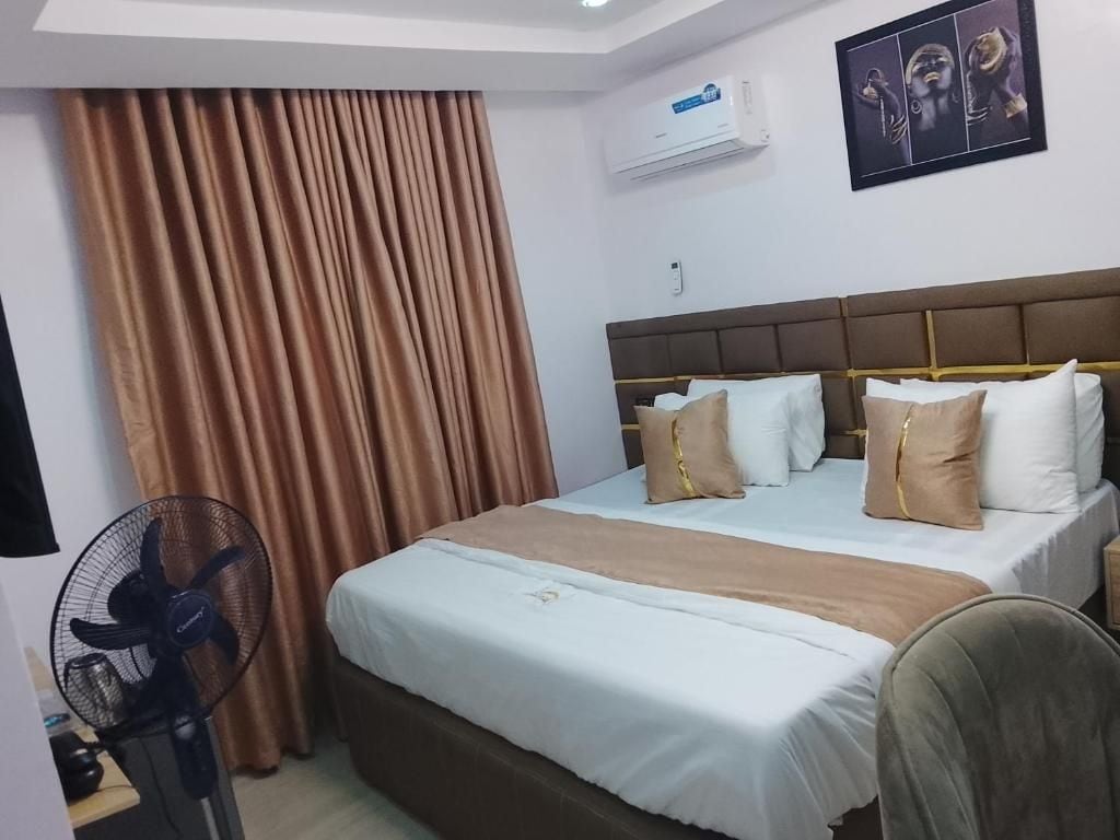 A hotel room with a bed, curtains, an air conditioner, and a fan.