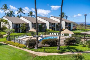 A hotel with multiple-story buildings, a swimming pool, and a well-maintained garden with palm trees and yellow flowers. - Tropical Kihei 1bd Across from Kamaole Beach (Kihei)