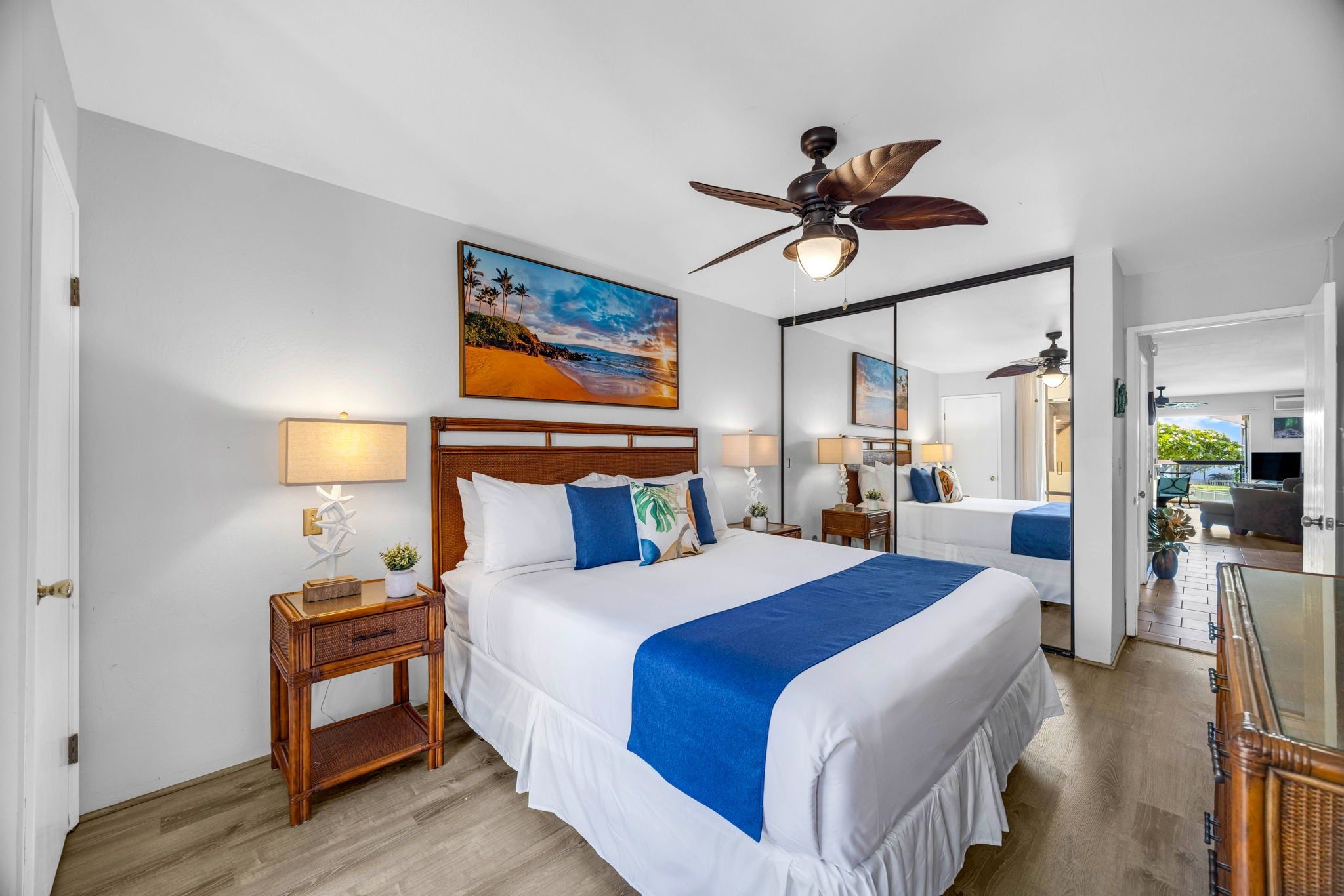 A hotel room with a large bed, two bedside tables, a ceiling fan, a painting, and a mirror.