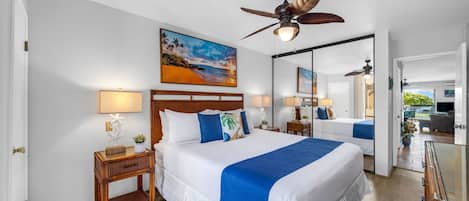 Une chambre d’hôtel avec un grand lit, deux tables de chevet, un ventilateur de plafond, un tableau et un miroir.