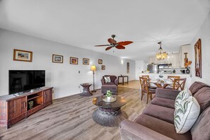 Ein modernes Wohnzimmer mit Flachbildfernseher, rundem Couchtisch, einer Couch und einem Essbereich mit Stühlen.