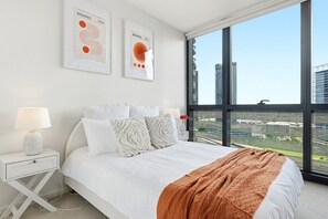 A modern bedroom with a large bed, white bedding, and two framed abstract art pieces on the wall. - Waterfront Escape 2BR Apt w/Pool, Gym & Parking (Docklands)