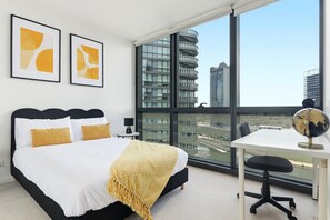 A modern bedroom with a large bed, a desk, and a view of a cityscape through large windows. - Waterfront Escape 2BR Apt w/Pool, Gym & Parking (Docklands)