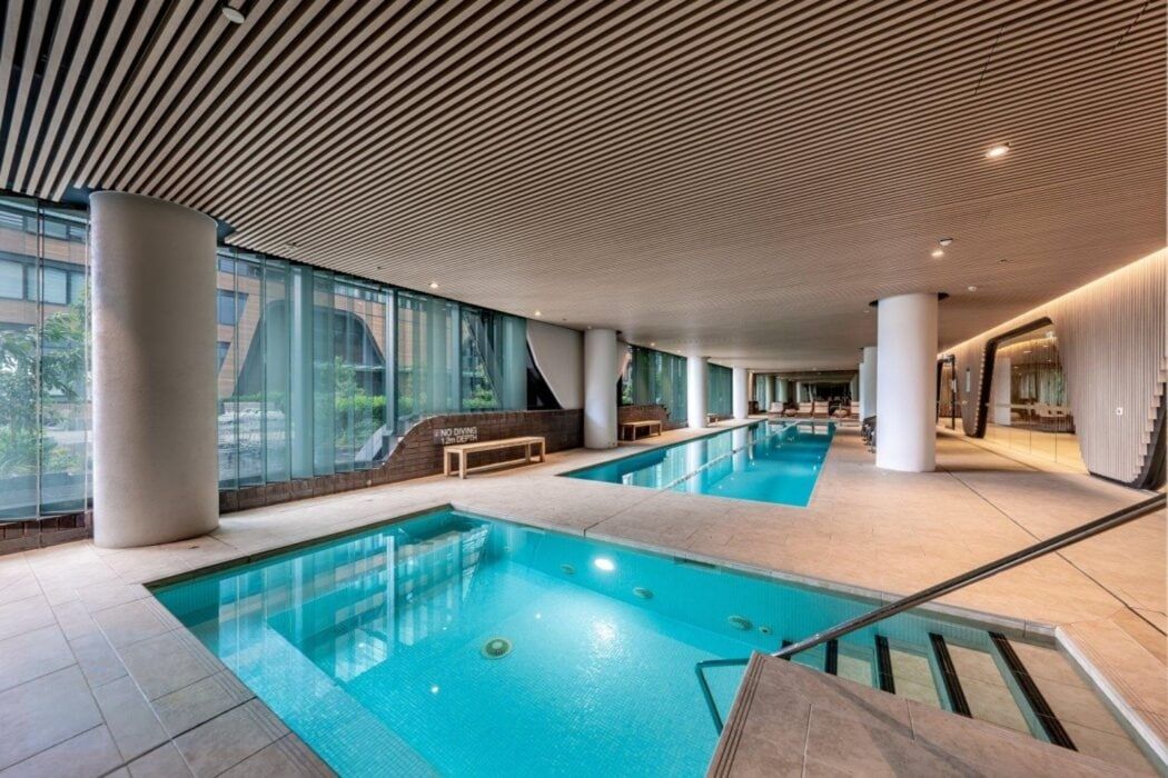 Un espace piscine intérieure doté de murs en verre transparent, de plusieurs bassins et d’un design de plafond moderne.