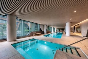 Zona de piscina interior amb parets de vidre transparent, diverses piscines i un disseny de sostre modern.
