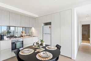 A modern kitchen with a dining table set for four, a built-in oven, and a refrigerator. - Waterfront Escape 2BR Apt w/Pool, Gym & Parking (Docklands)