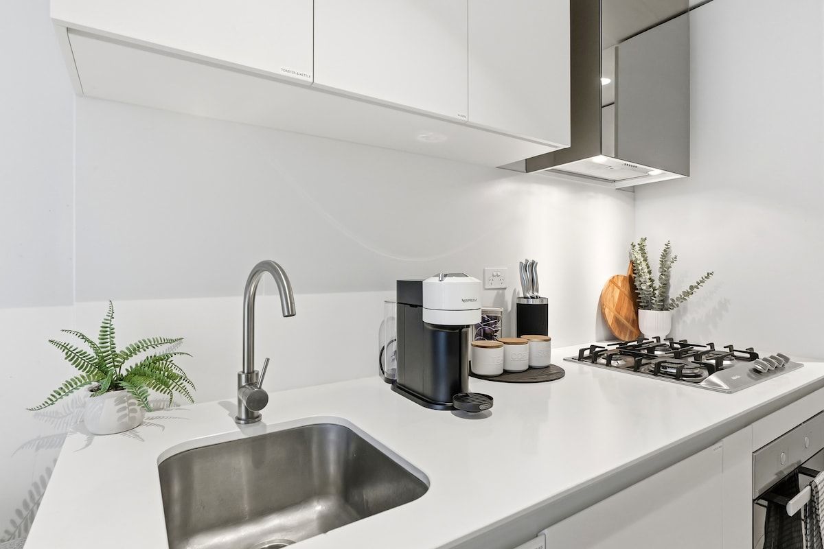 Une cuisine moderne équipée d’un évier en acier inoxydable, d’une machine à café et d’une cuisinière à gaz.