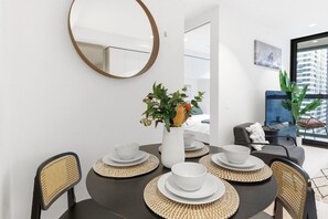 Ein Essbereich mit einem runden Tisch, gedeckt für vier Personen, einer Blumenvase und einem modernen Spiegel an der Wand.