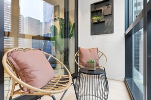 Een balkon met rieten stoelen, een tafeltje en een plank met planten.