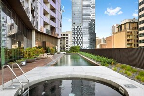 A modern building with a swimming pool, surrounded by other high-rise buildings. - Highrise CBD Stay | 2B2B Apt w/Pool & Gym (Melbourne)