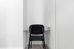 Une chaise noire se trouve dans un coin d’une pièce aux murs blancs et à l’étagère en bois.