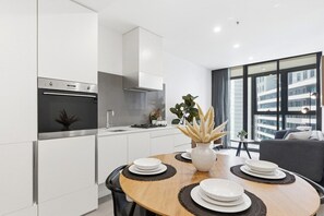 A modern kitchen with white cabinetry, a built-in oven, and a dining area with a round table set for four. - Cosy 2BR apartment close to Melbourne Exhibition Centre and Crown (Southbank)