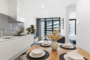 A modern kitchen with white cabinets, a stainless steel range hood, and a dining area with a wooden table set for four. - Cosy 2BR apartment close to Melbourne Exhibition Centre and Crown (Southbank)