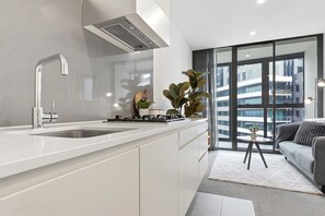 A modern kitchen with a built-in sink, a stove, and a range hood. There is a large window providing a view of the cityscape. - Cosy 2BR apartment close to Melbourne Exhibition Centre and Crown (Southbank)