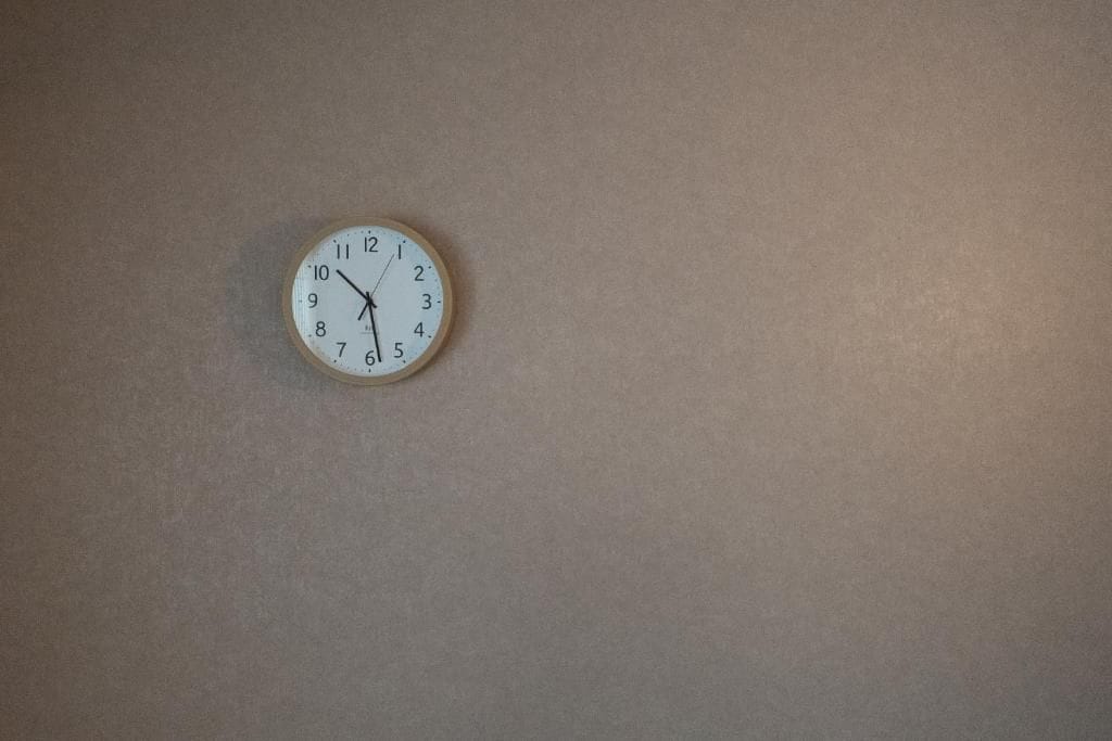 Relógio fixado na parede, com mostrador branco e números pretos.