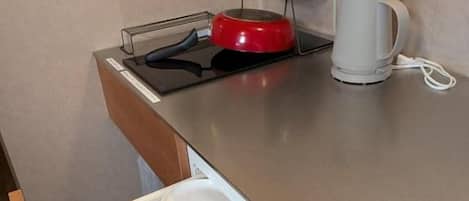 A kitchen with a countertop, a kettle, a pot, and a drawer with dishes.