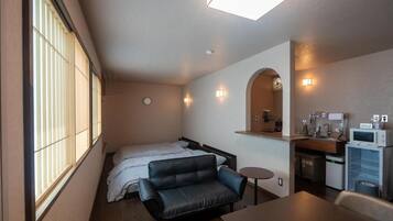 Una habitación compacta con cama, sofá, una mesita, microondas y lavamanos.