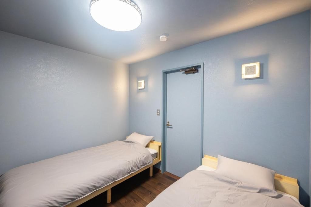 Una habitación con dos camas individuales, una puerta y una lámpara.