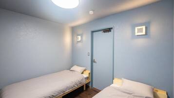 Una habitación con dos camas individuales, una puerta y una lámpara.