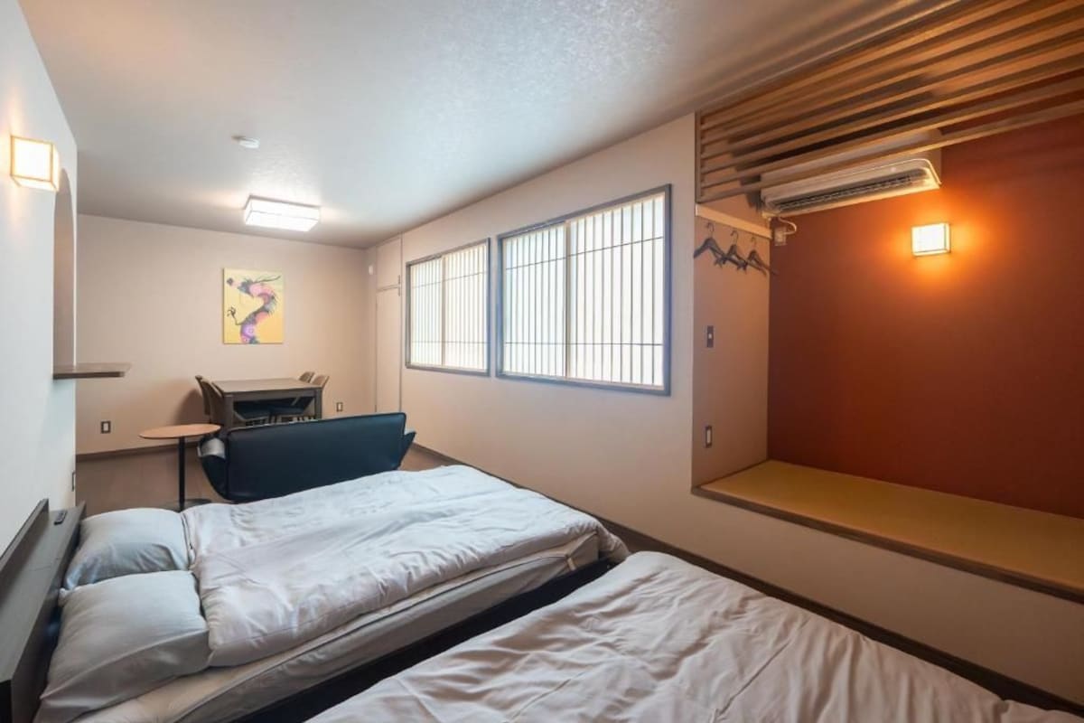 A hotel room with two beds, a desk, and a window with blinds.